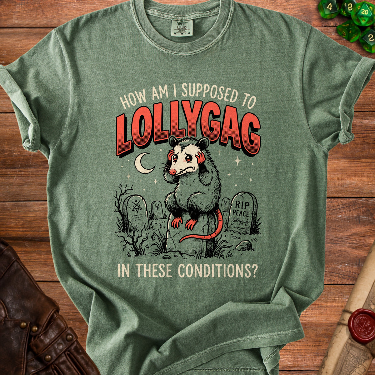 Green t-shirt with opossum graphic and text "How Am I Supposed To Lollygag In These Conditions?".