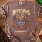 Brown t-shirt with "Brew Intentions Questionable Spells" graphic of witches and cauldron.