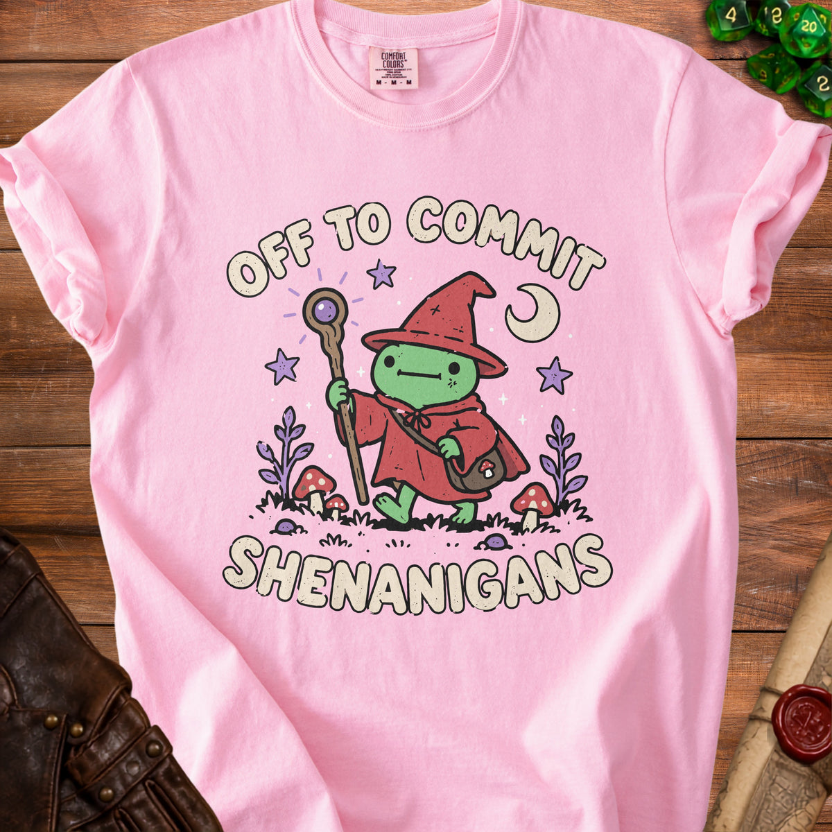 Pink t-shirt with cartoon wizard frog, stars, moon, mushrooms, and text "OFF TO COMMIT SHENANIGANS".