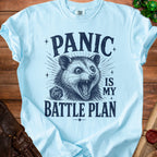Light blue t-shirt with possum graphic and text "Panic is my battle plan".