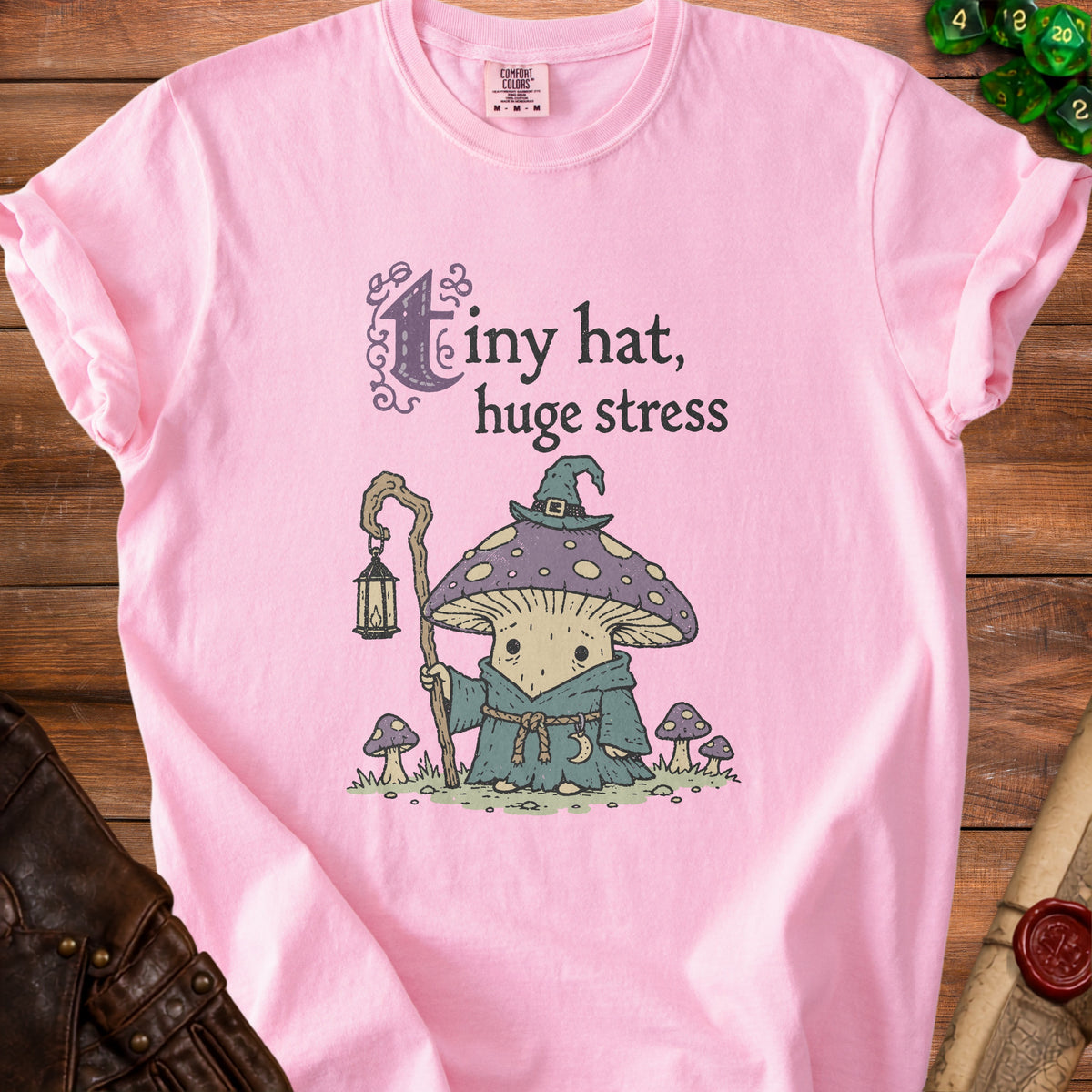 Pink t-shirt with a mushroom wizard illustration and text "tiny hat, huge stress".