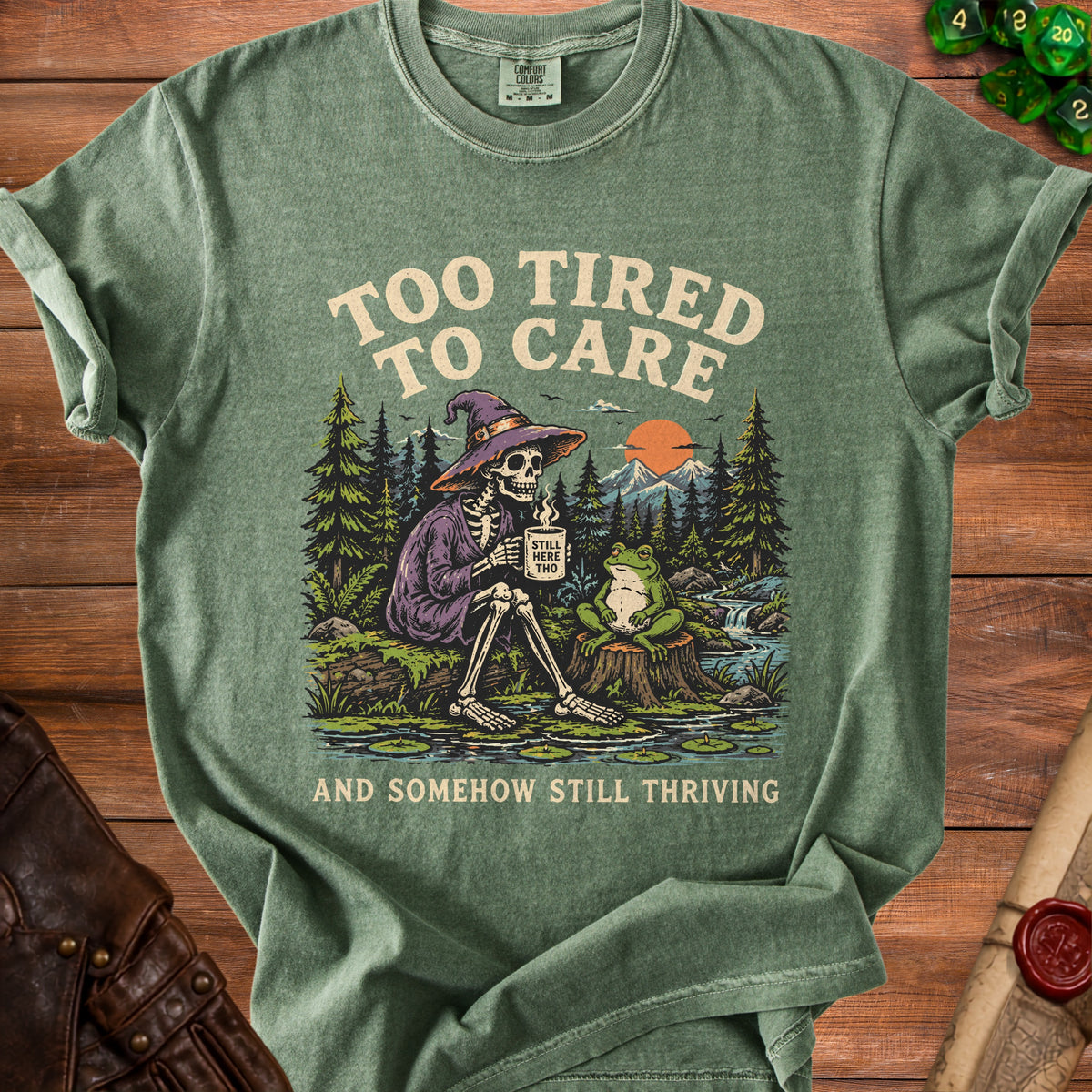 Skeleton in witch hat drinks coffee with a frog, text "Too Tired To Care" and "And Somehow Still Thriving".