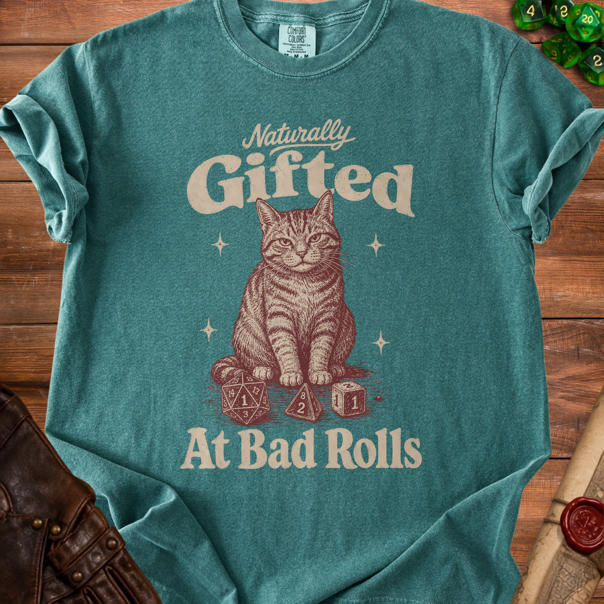 Teal t-shirt with a tabby cat and dice graphic that reads "Naturally Gifted At Bad Rolls."