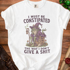White t-shirt with green goblin graphic and text "I MUST BE CONSTIPATED THE WAY I DON'T GIVE A SHIT".