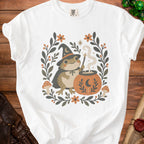 Frog in witch hat stirring cauldron surrounded by floral and mushroom border.
