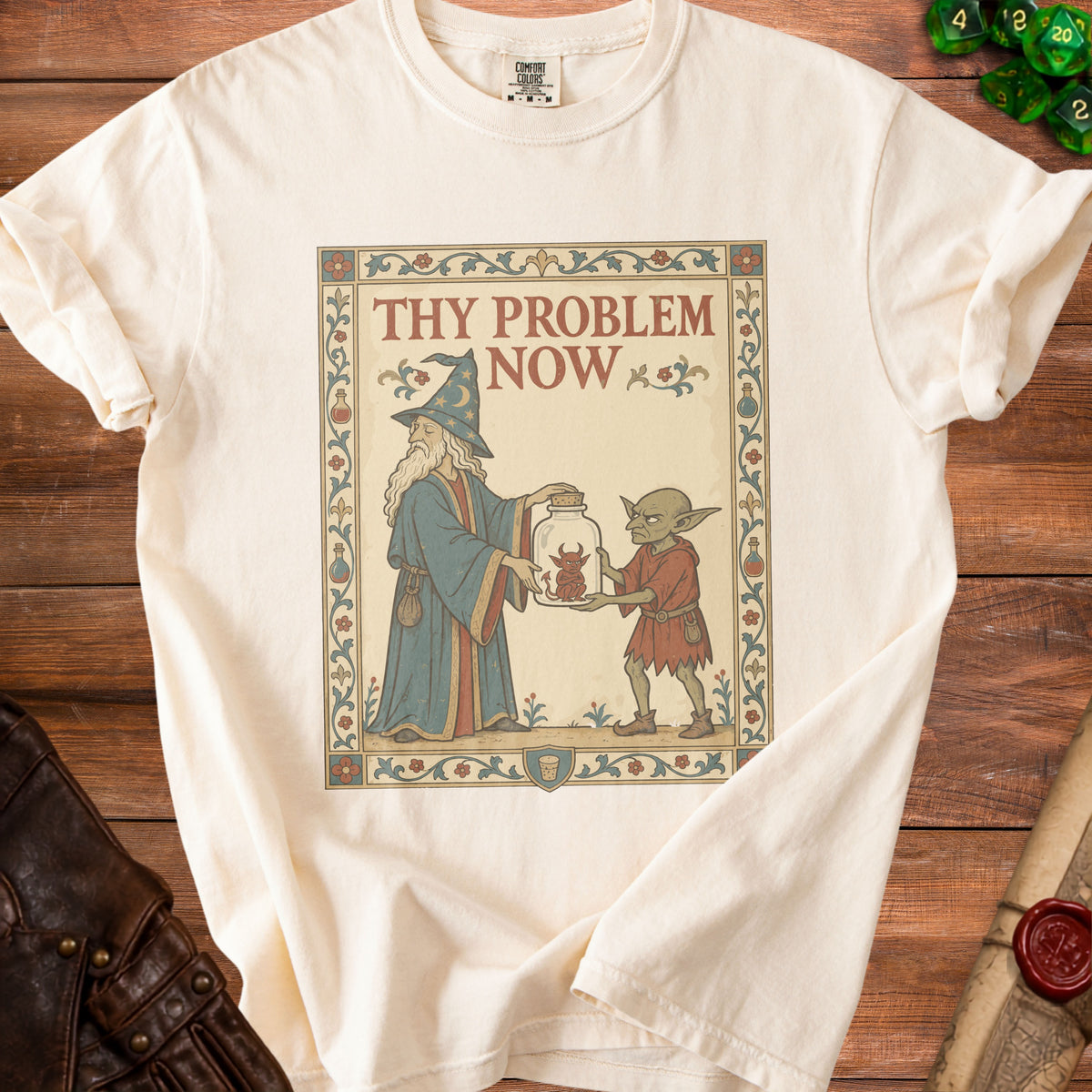 Cream t-shirt with a medieval-style graphic of a wizard and goblin holding a jar with a devil.