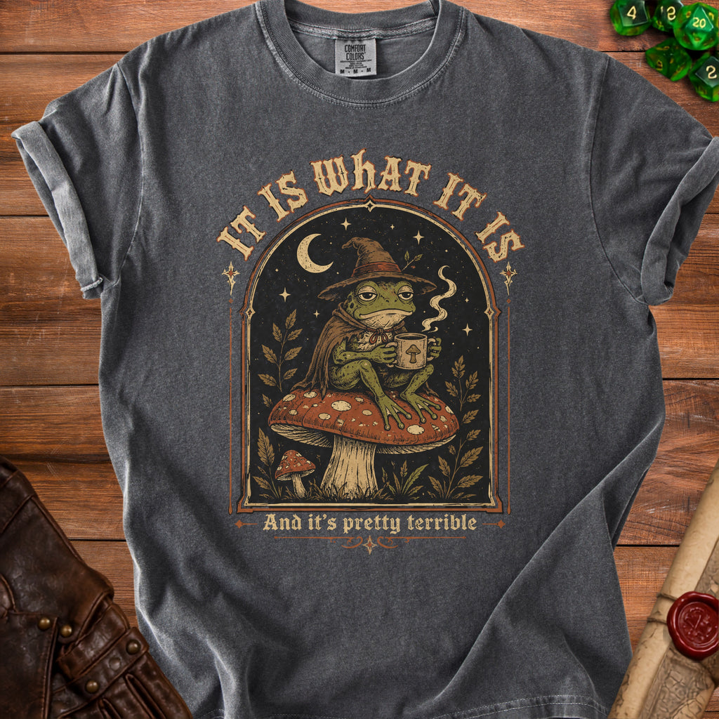Frog in a witch hat sits on a mushroom holding a mug, "It is what it is."