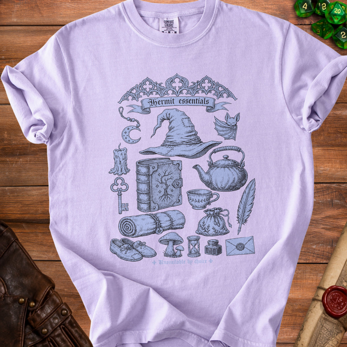 Lilac t-shirt with "Hermit essentials" graphic featuring wizard hat and various magical items.
