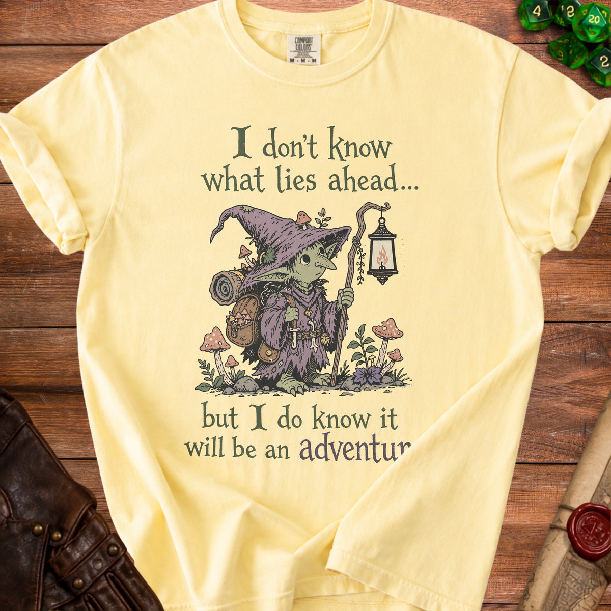Yellow t-shirt with illustration of a goblin, lantern, and text "I don't know what lies ahead... but I do know it will be an adventure".