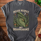 Dark grey t-shirt with a graphic of a frog peeking from a leaf and text "PLEASE RESPECT MY DISAPPEARANCE".