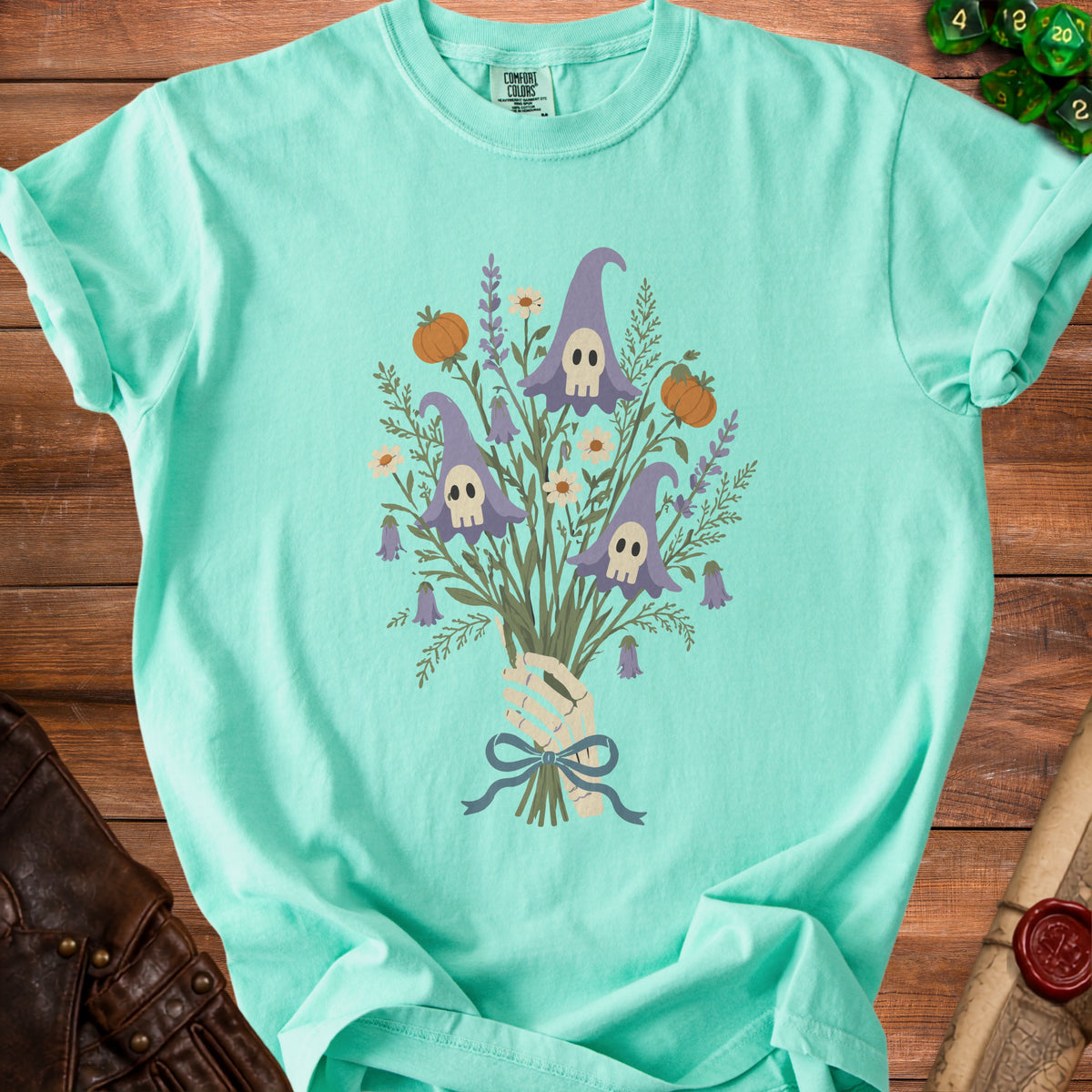 Mint green t-shirt with a skeleton hand holding a bouquet of witch hats, pumpkins, and flowers.