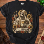 Skeleton wearing armor and robes holding potion and book, surrounded by flowers, text "Still Healing".