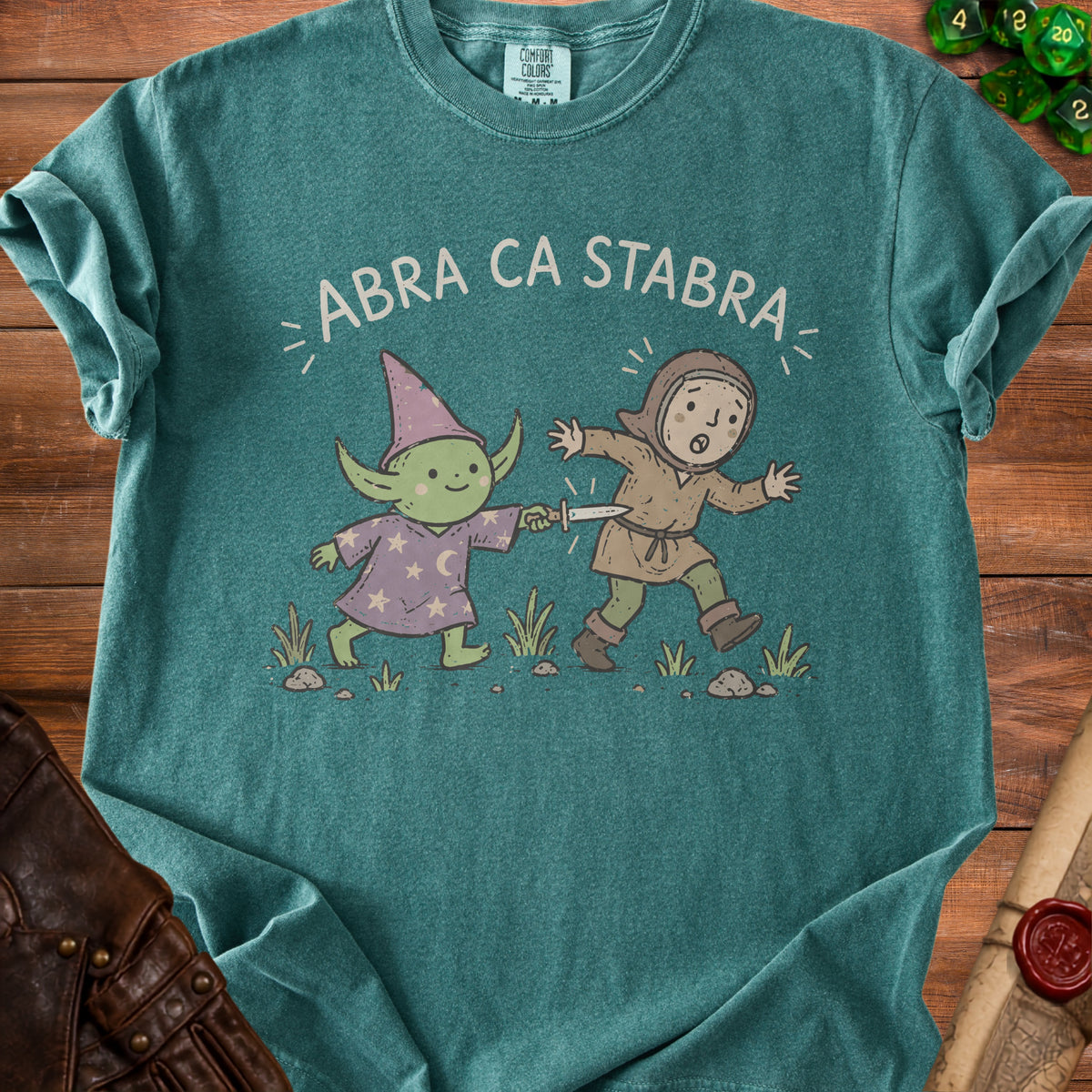 Teal t-shirt with "ABRA CA STABRA" and illustration of a wizard stabbing a surprised character.