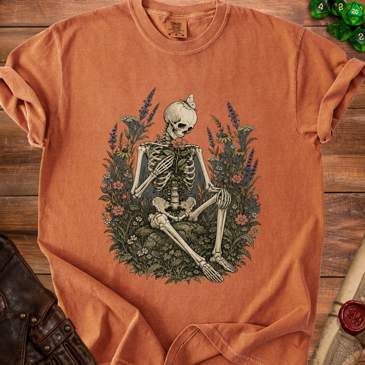 Orange t-shirt with skeleton holding flower and butterfly, surrounded by foliage.