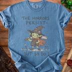 Blue t-shirt with illustration of a goblin witch holding knives, text reads "THE HORRORS PERSIST- BUT SO DO I".