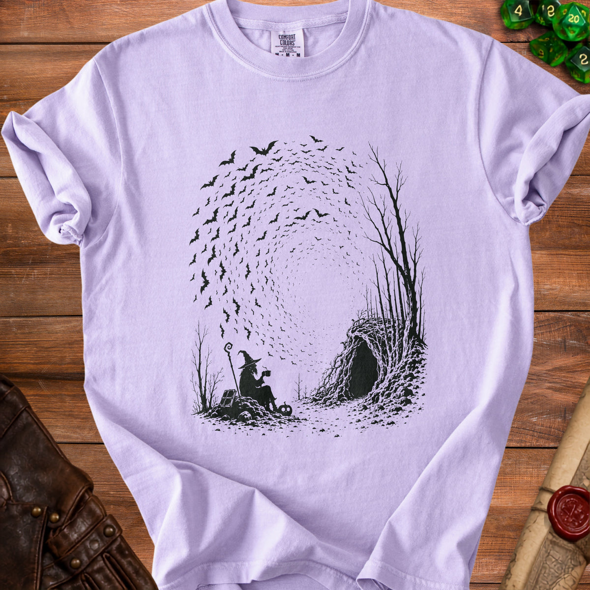 Purple t-shirt with a black graphic of a witch and bats by a cave entrance.