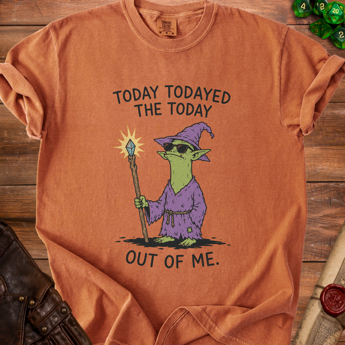 Orange t-shirt with a graphic of a green goblin wearing a hat, sunglasses, and robe, holding a staff.