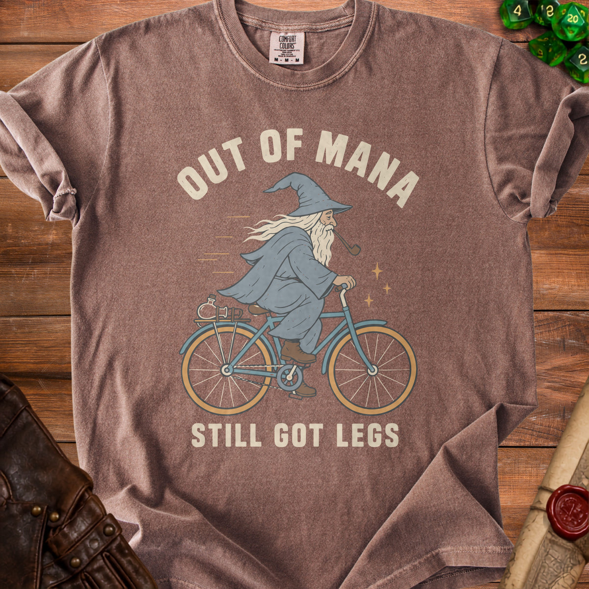 Brown t-shirt with graphic of wizard riding bicycle, text "OUT OF MANA STILL GOT LEGS".