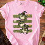 Pink t-shirt with three green cartoon frogs wearing witch hats.