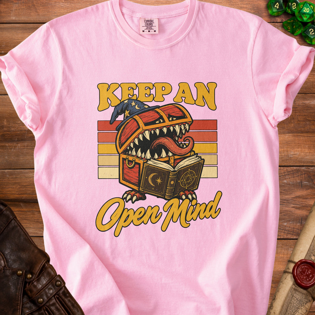 Pink t-shirt with a graphic of a treasure chest monster reading a book, text "Keep an Open Mind".