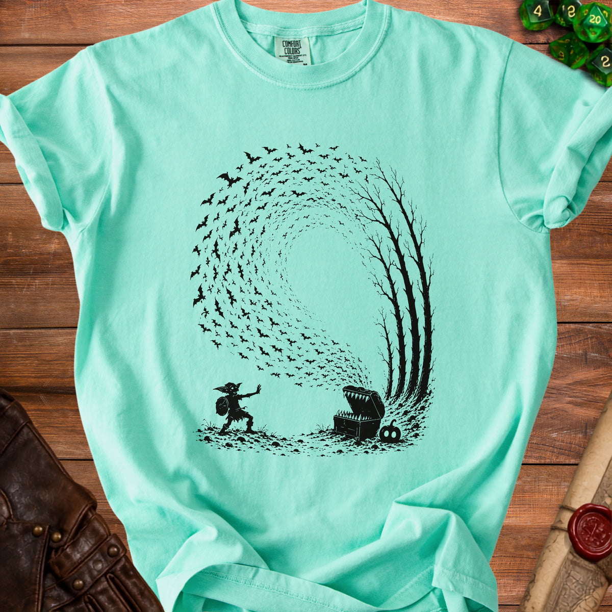 Mint t-shirt with black graphic of a goblin facing a treasure chest with bats flying around trees.