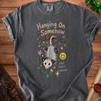 Dark grey t-shirt with a graphic of an opossum hanging from a branch and text.