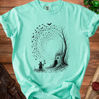 Mint t-shirt with black print of a horned figure and a tree with a face.
