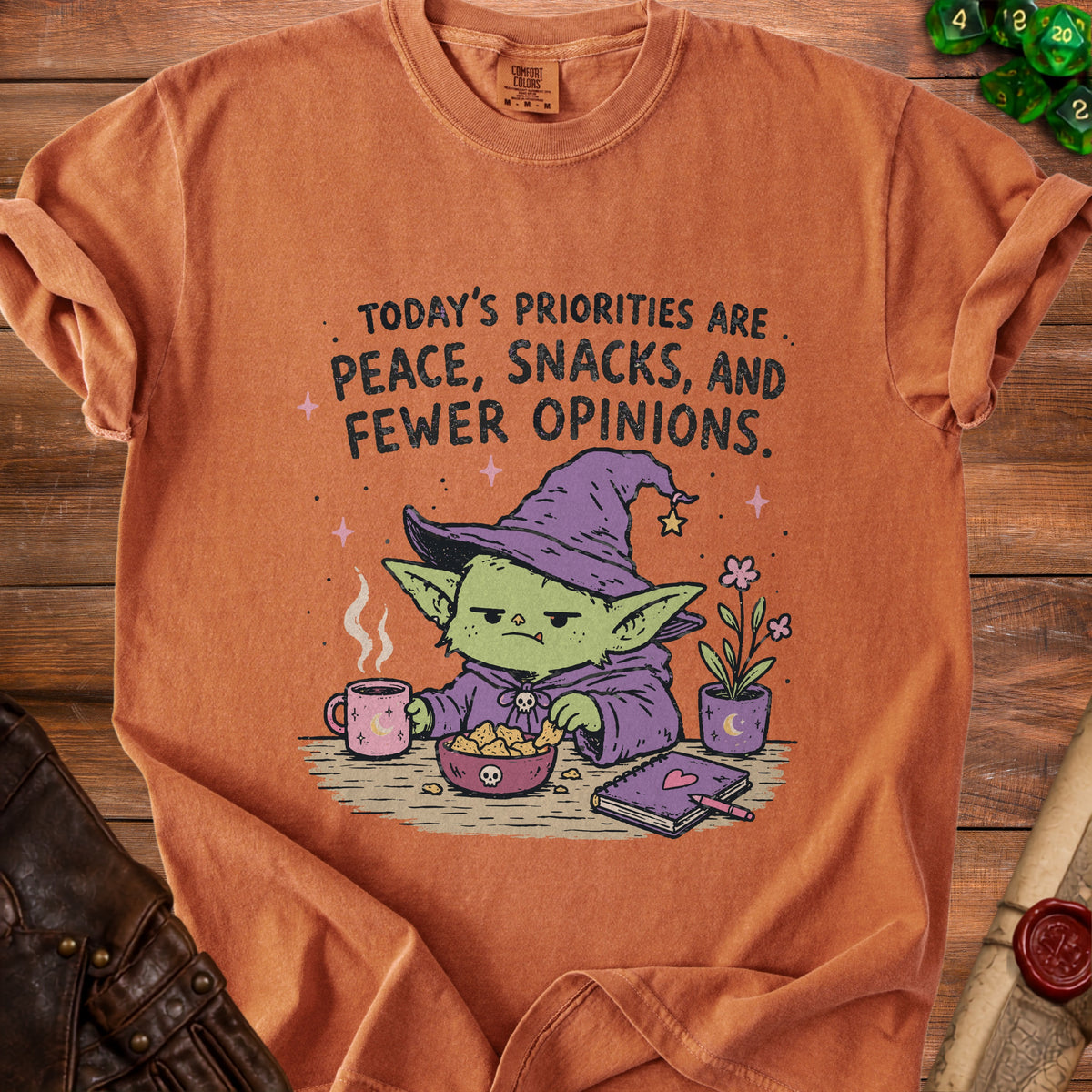 Orange t-shirt with cartoon witch eating snacks and text "Today's Priorities Are Peace, Snacks, and Fewer Opinions."