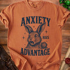Orange t-shirt with distressed print of a rabbit, dice, and text reading "ANXIETY HAS ADVANTAGE".