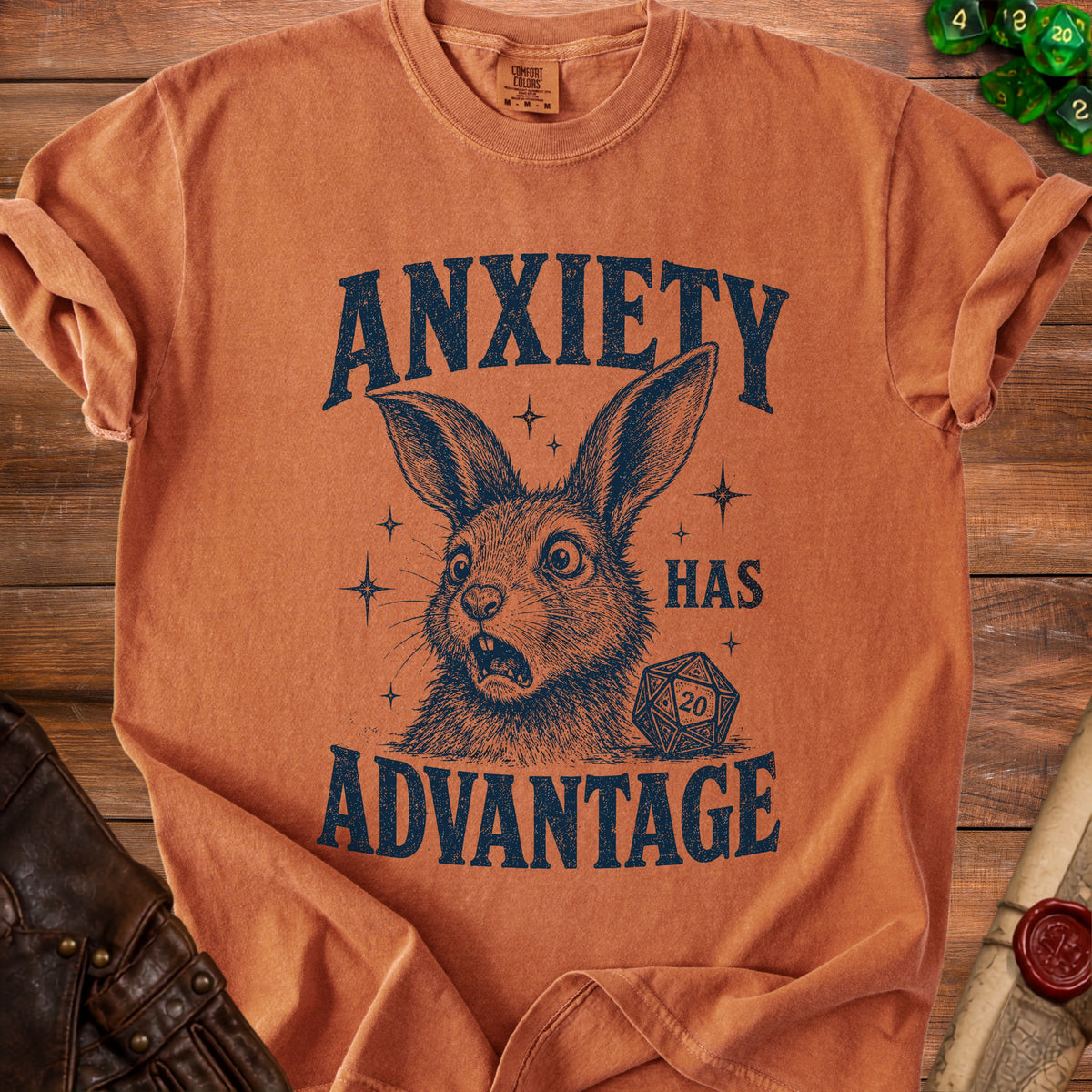 Orange t-shirt with distressed print of a rabbit, dice, and text reading "ANXIETY HAS ADVANTAGE".