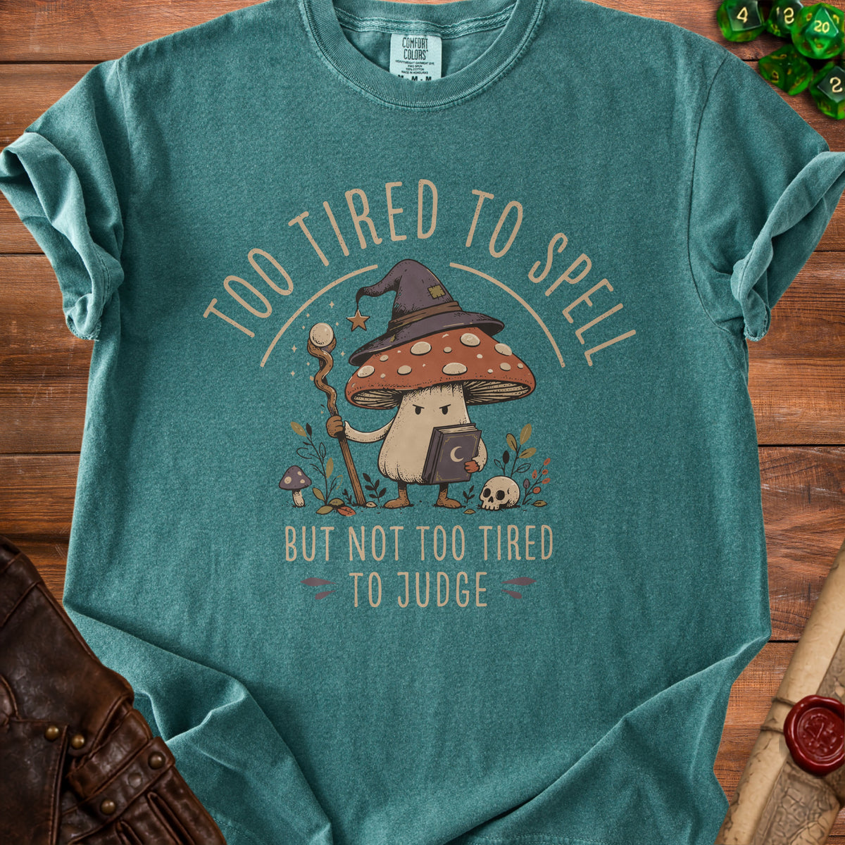 Teal t-shirt with wizard mushroom graphic and text "Too Tired To Spell But Not Too Tired To Judge".