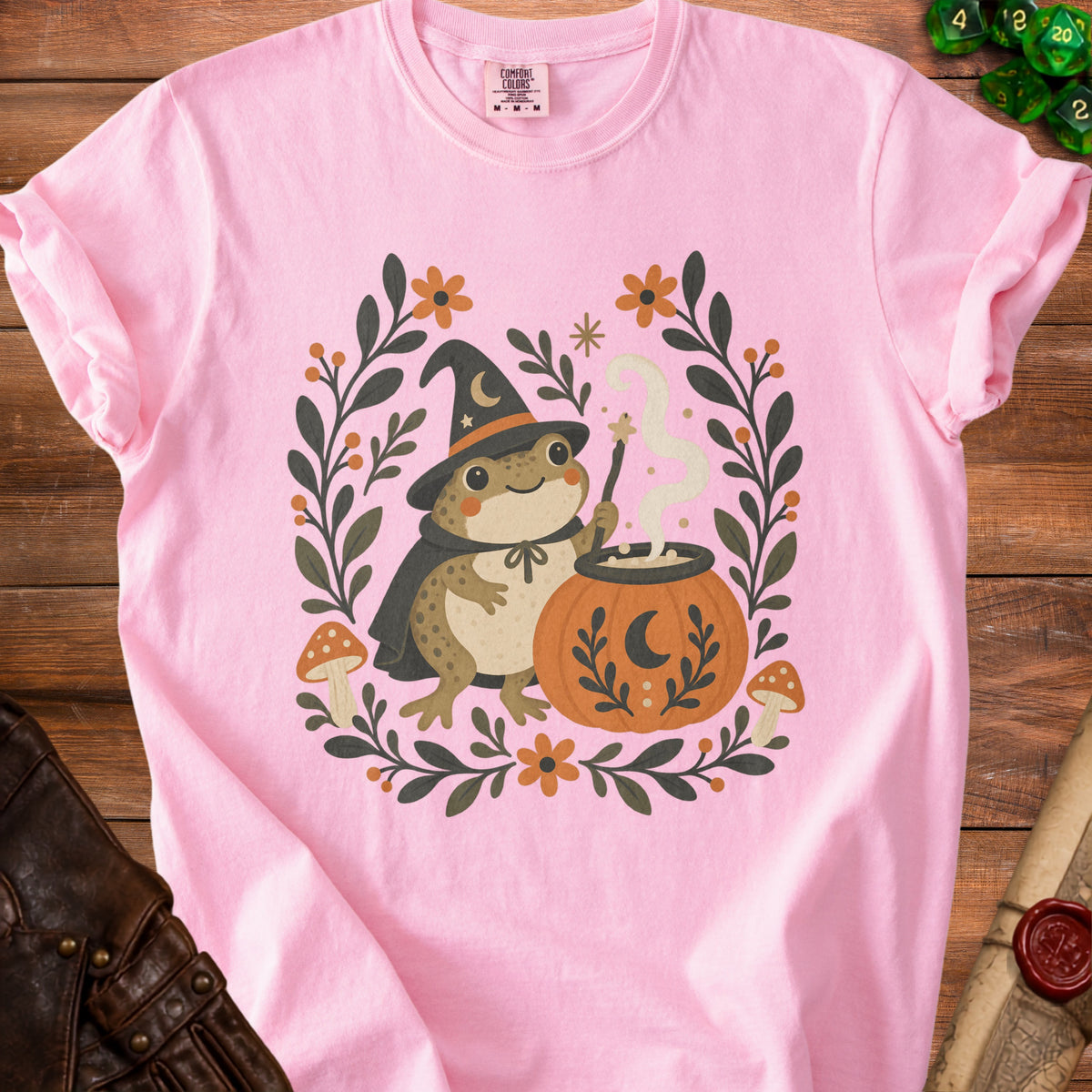 Pink t-shirt with a smiling frog wizard casting a spell on a cauldron.