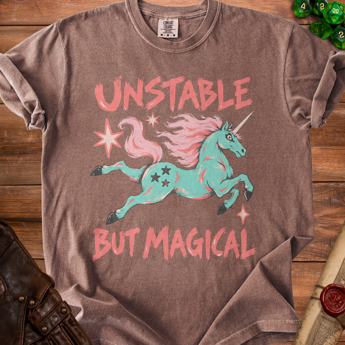 Brown t-shirt with a mint green unicorn and pink text "UNSTABLE BUT MAGICAL."