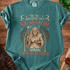 Teal t-shirt with "Be The Ancestor They Summon" and a witch graphic.