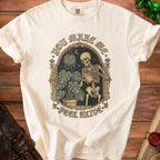 Cream t-shirt with skeleton watering plants graphic and text "You Make Me Feel Alive".