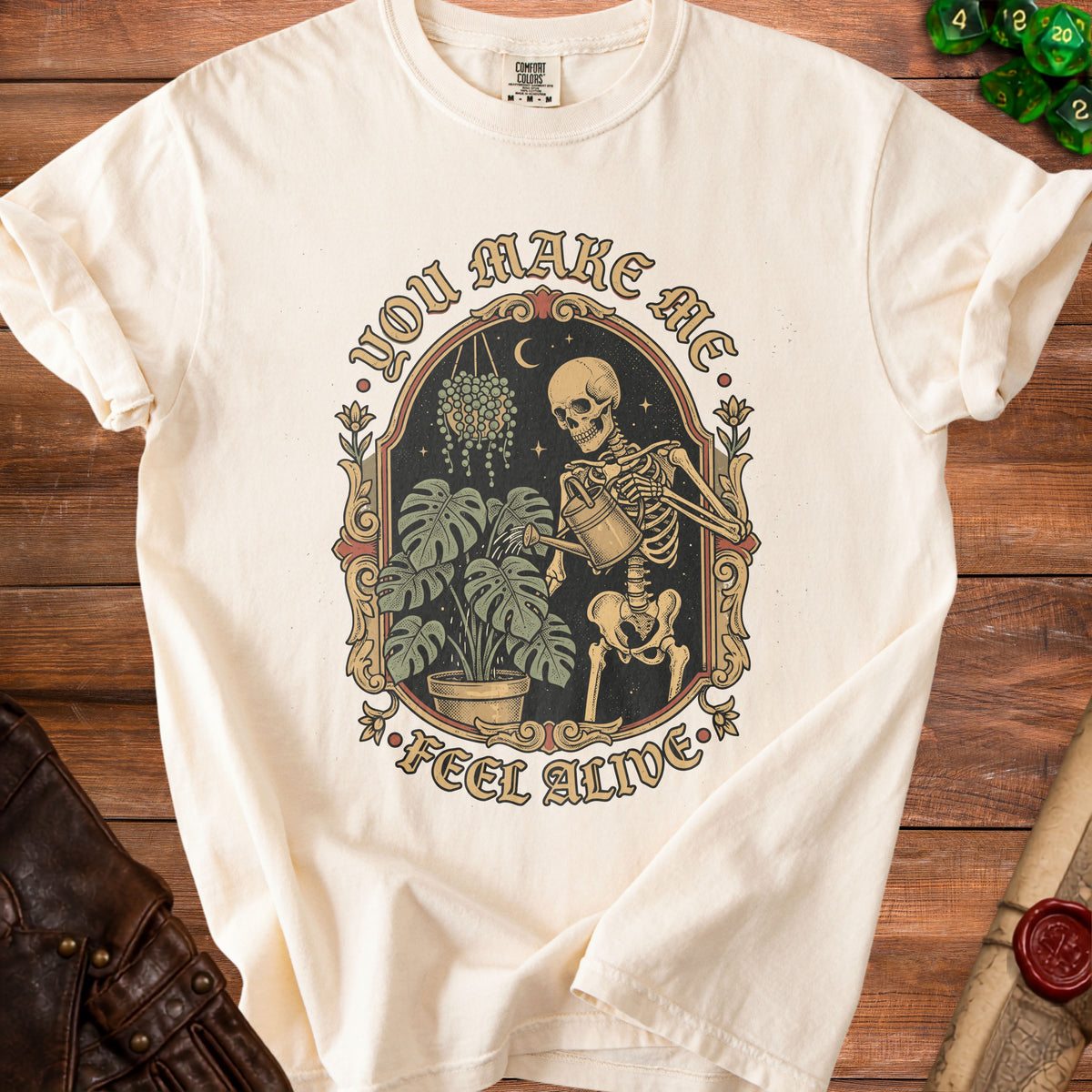 Cream t-shirt with skeleton watering plants graphic and text "You Make Me Feel Alive".