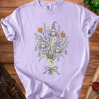 Lavender t-shirt with skeleton hand holding a bouquet of spooky ghosts and pumpkins.