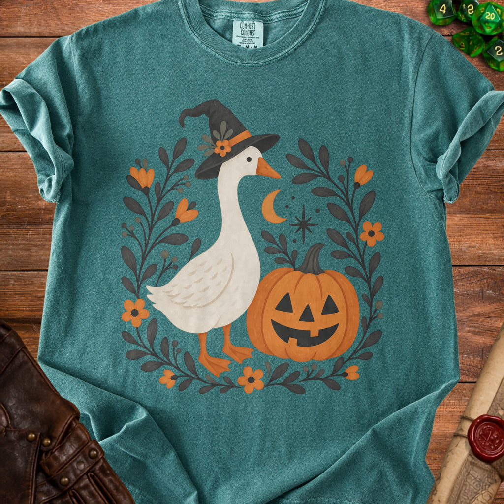 Teal t-shirt with white goose in witch hat next to jack-o'-lantern.