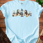 Light blue t-shirt with cartoon ducks dressed as adventurers sitting around a campfire.