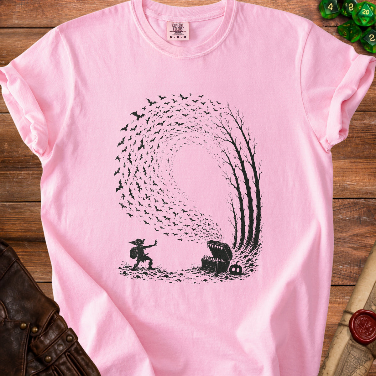 Pink t-shirt with black graphic of a goblin, open treasure chest, and swarming bats.