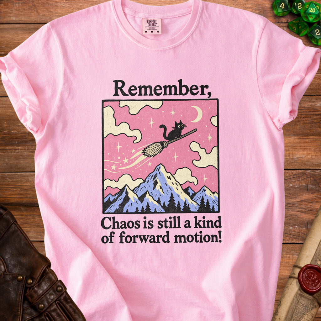 Pink t-shirt with graphic of black cat on broom over mountains, text "Remember, Chaos is still a kind of forward motion!"