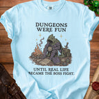 Light blue t-shirt with graphic of tired hooded figure and text "Dungeons Were Fun Until Real Life Became the Boss Fight."