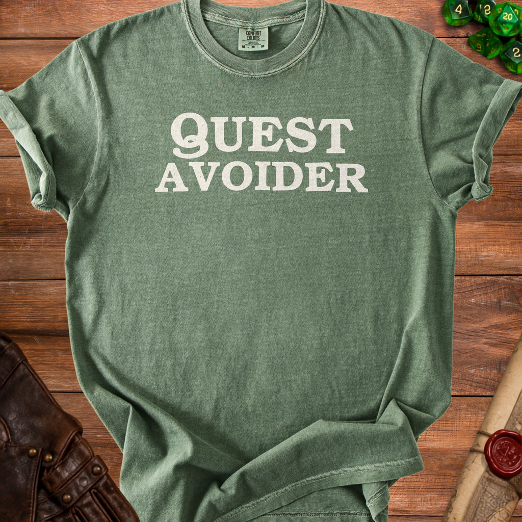 Green t-shirt with white text "QUEST AVOIDER" on a wooden surface.