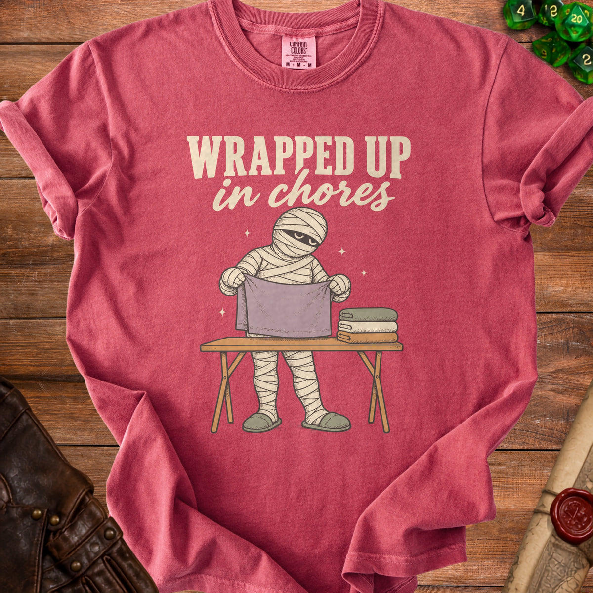 Mummy folding laundry with text "Wrapped Up in Chores" on shirt.