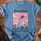 Blue t-shirt with a black cat flying on a broom over mountains, text "Remember, Chaos is still a kind of forward motion!".