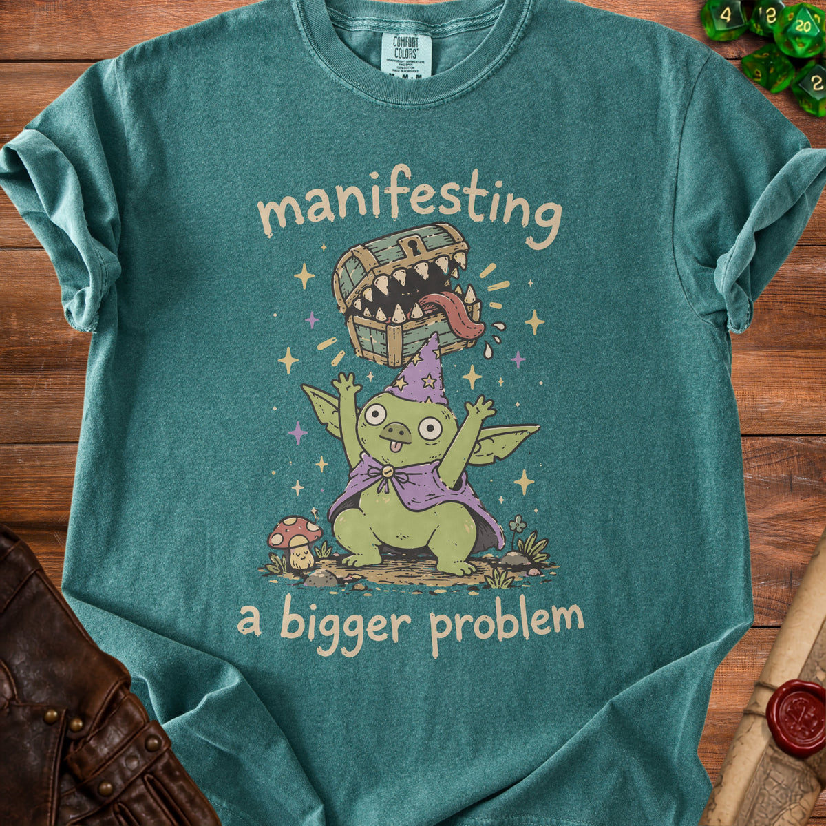Green t-shirt with a goblin wearing a wizard hat and a treasure chest that says "manifesting a bigger problem".