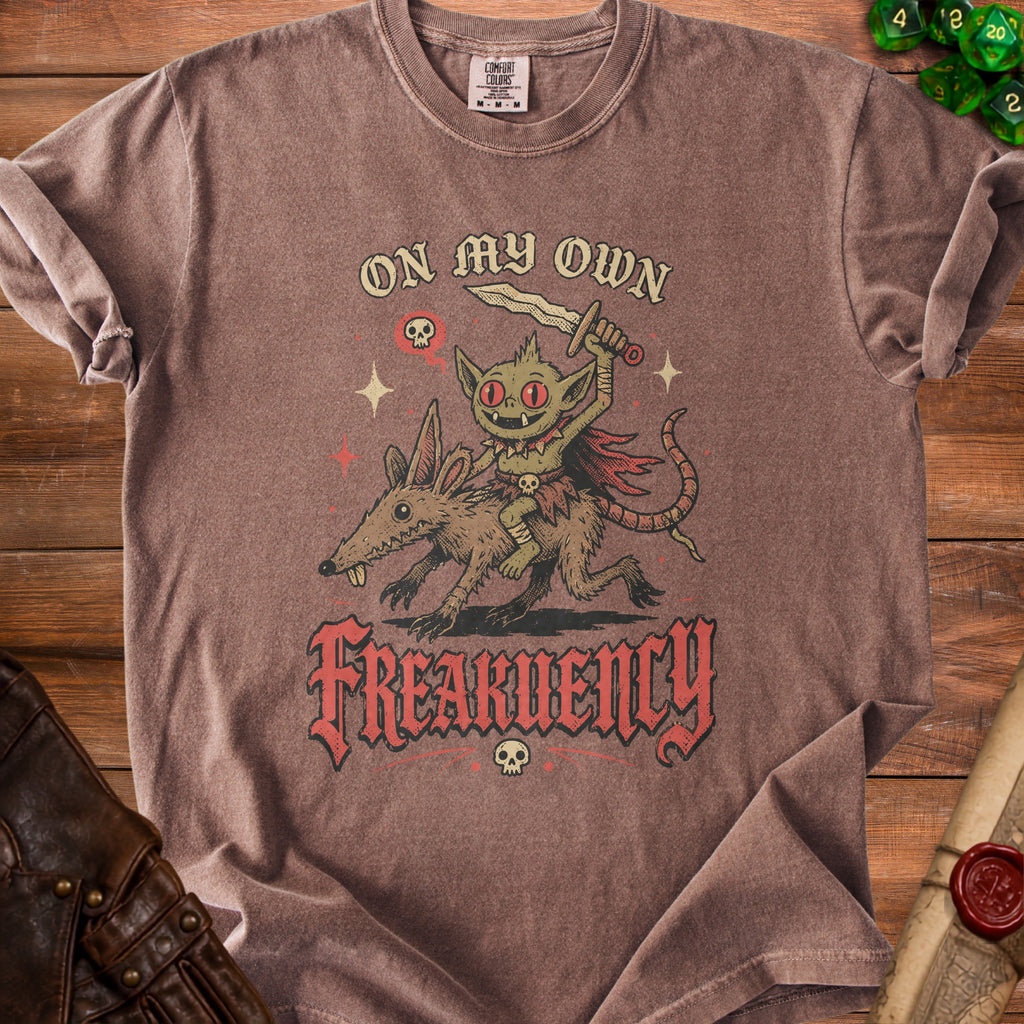 Brown t-shirt with a goblin riding a rat and text reading "ON MY OWN FREAKUENCY".