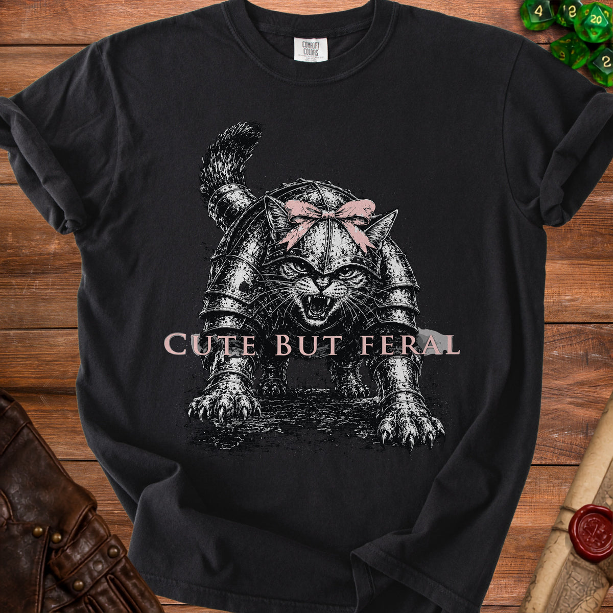 Black t-shirt with a fierce cat in armor wearing a pink bow and text "CUTE BUT FERAL".