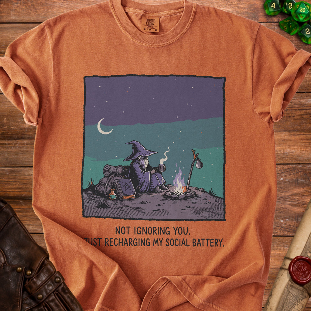 Orange t-shirt with wizard by campfire graphic and text "NOT IGNORING YOU. JUST RECHARGING MY SOCIAL BATTERY."
