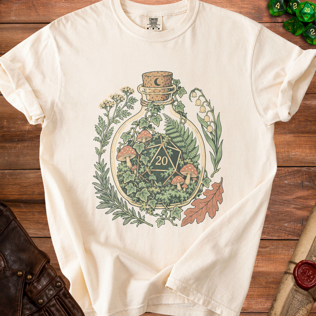 Cream t-shirt with a glass bottle graphic containing a D20 dice, mushrooms, and foliage.